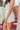 Side view of model wearing the Once In A Lifetime Pleated Shorts that feature white pleated fabric, white shorts lining, and a monochromatic back zipper with a hook closure
