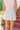 Back view of model wearing the Once In A Lifetime Pleated Shorts that feature white pleated fabric, white shorts lining, and a monochromatic back zipper with a hook closure