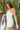 Side view of model wearing the Happiest With You Romper that has white denim fabric, a scooped skirt design with ruched detailing on the side, white shorts lining, a strapless sweetheart neck, and a back zipper with hook closure