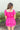Back view of model wearing the Wishful Thinking Romper which features fuchsia fabric, a ruffle-tiered skirt, fuchsia shorts lining, an elastic waistband, a sweetheart neckline and short puff sleeves.