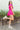 Full body side view of model wearing the Wishful Thinking Romper which features fuchsia fabric, a ruffle-tiered skirt, fuchsia shorts lining, an elastic waistband, a sweetheart neckline and short puff sleeves.