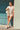 Full body view of model wearing the Dakota Denim Romper in Off White which features white denim fabric, front pockets, a hidden front zipper, a collared neckline, a monochromatic belt at the waistline, and short sleeves.