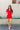Full body view of model wearing the Dakota Denim Romper in Red which features red denim fabric, front pockets, a hidden front zipper, a collared neckline, a monochromatic belt at the waistline, and short sleeves.