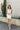 Full body view of model wearing the Starlight Rhinestone Fringe Dress in White which features white fabric, a straight neckline, a sleeveless design with thin adjustable straps, rhinestone fringe detailing at the bottom side hem, criss cross straps in the