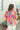 Back view of model wearing the Pop Of Color Blouse which features red fabric with a blue, orange, green, purple, pink and yellow print, a round neckline, a back keyhole with a button closure, and short flare sleeves.