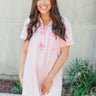 Front view of model wearing the Play It Cool Dress that has washed light pink fabric, one front chest pocket, a hidden quarter button-up, a v-neck with a collar, a frayed mini-length hem, and short sleeves.