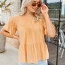 Front view of model wearing the Sunrise to Sunset Top which features orange fabric with a monochromatic stripe pattern, a tiered body, smocked details, a round neckline, short flare sleeves, and a back key hole with a button closure.