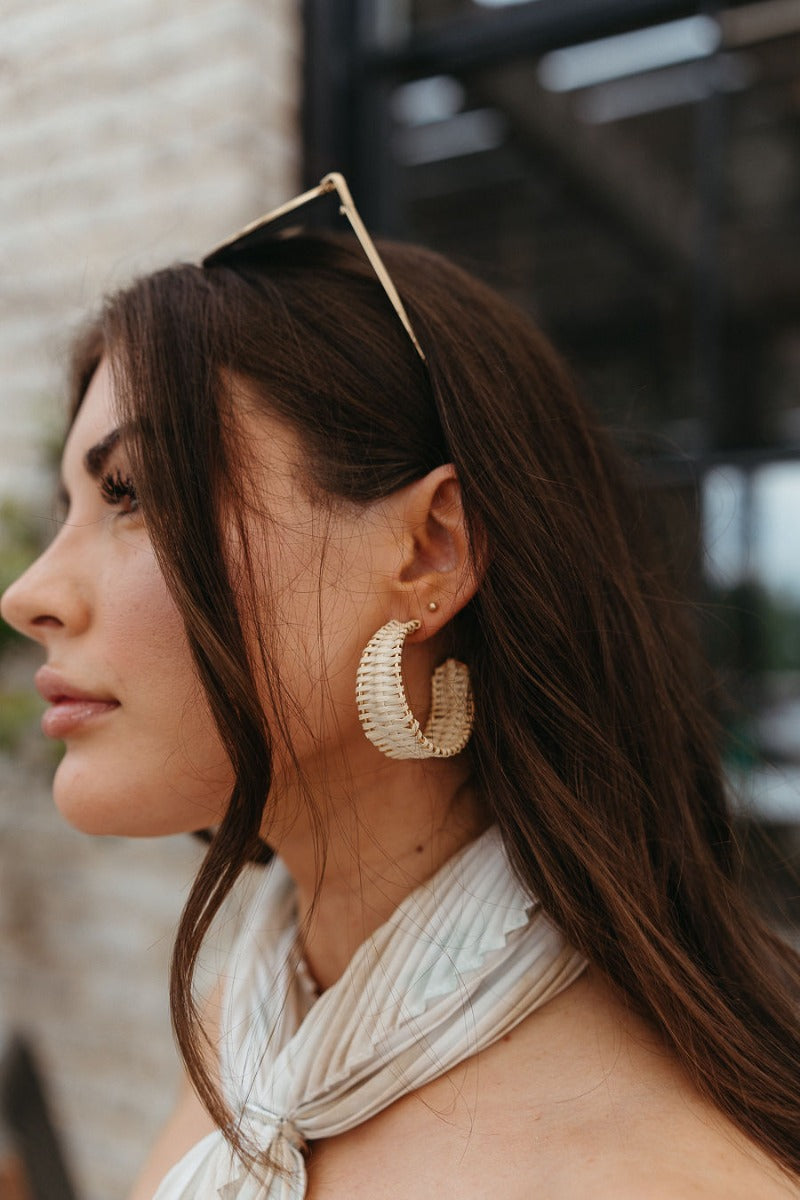 Side view of model wearing the To The Beach Earrings which features large, open gold hoop with natural raffia details.