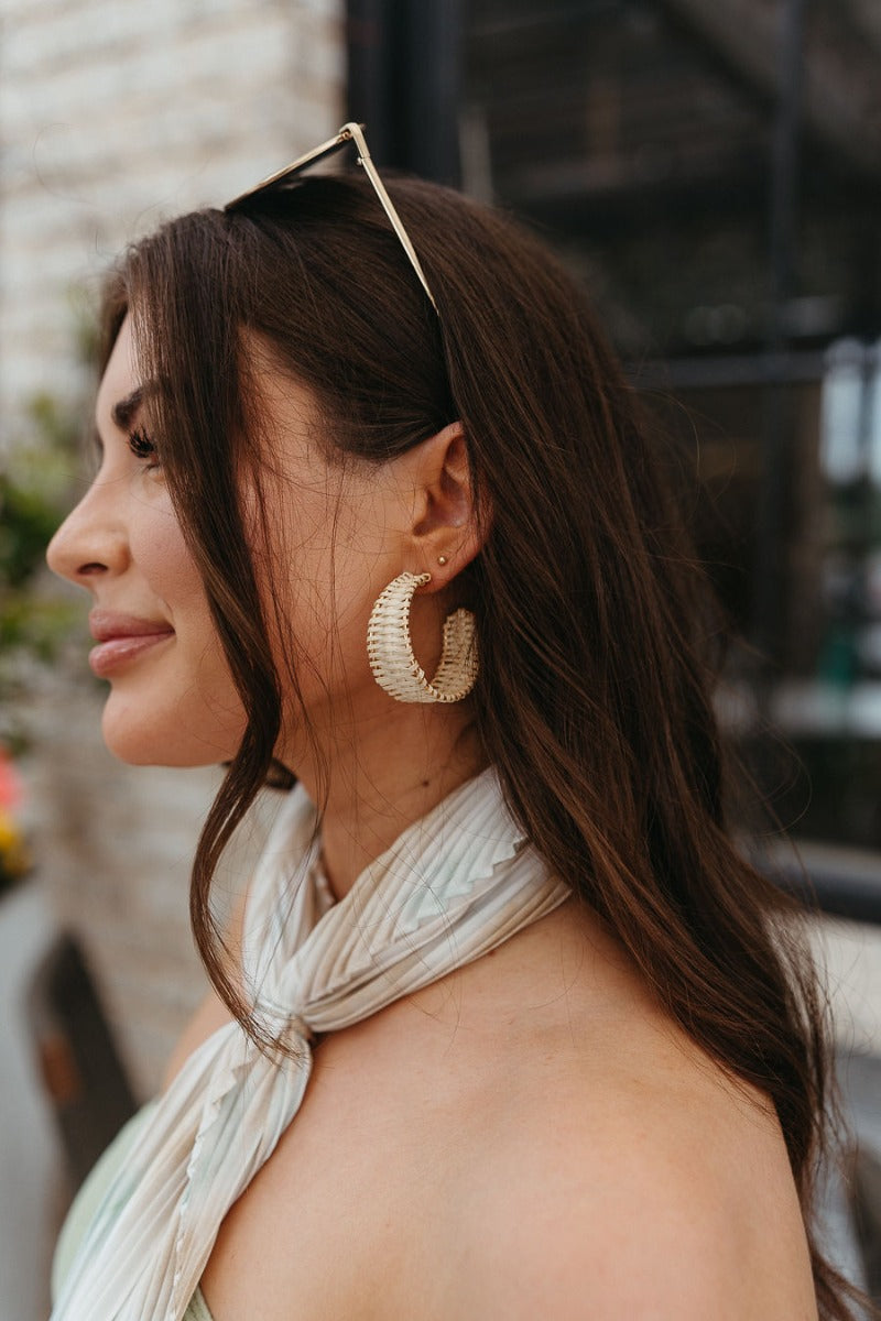 Side view of model wearing the To The Beach Earrings which features large, open gold hoop with natural raffia details.