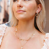 Front view of model wearing the Life Is Good Layered Necklace which features two-layered gold chain links with gold leaf attachments and teardrop shaped pearl medallion.