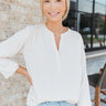 Front view of model wearing the Fresh Start Top which features cream fabric, a high-low hem, smocked details, a v-neckline, and long sleeves with elastic wrists.