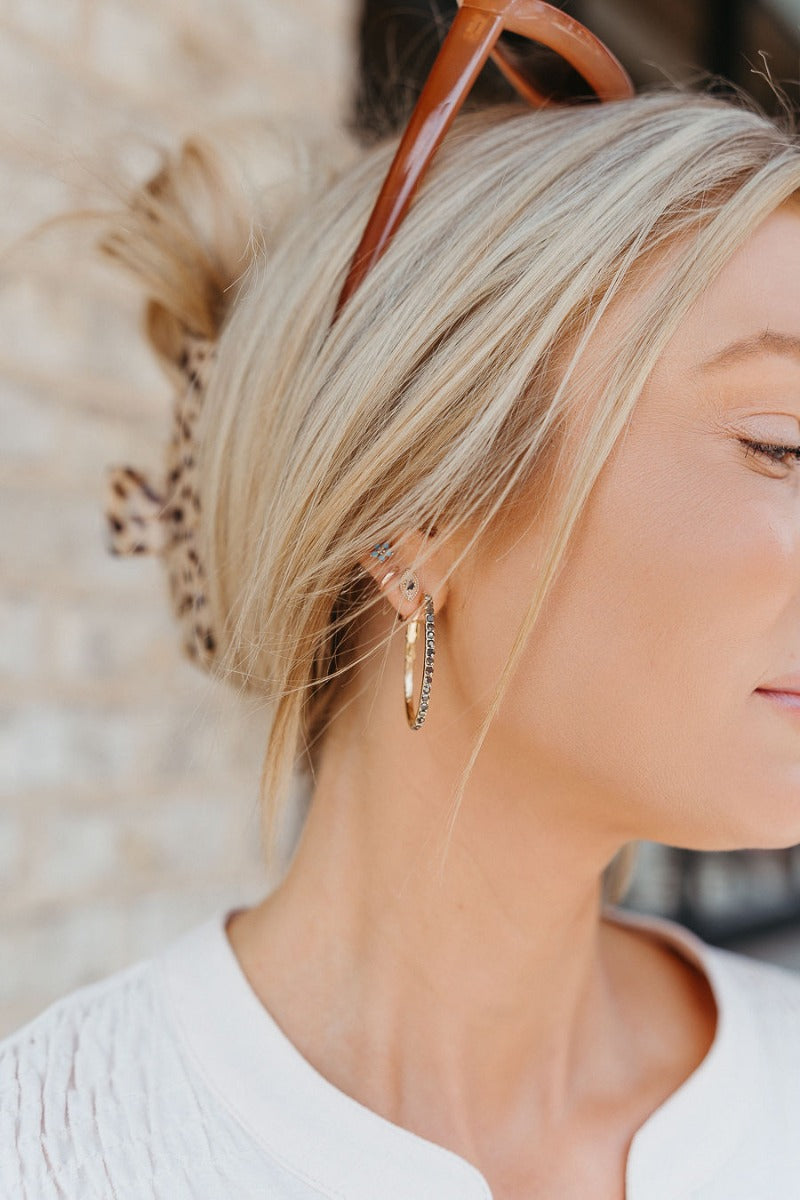Side view of model wearing the Should've Known Earrings which features gold scooped hoops with charcoal grey stones.
