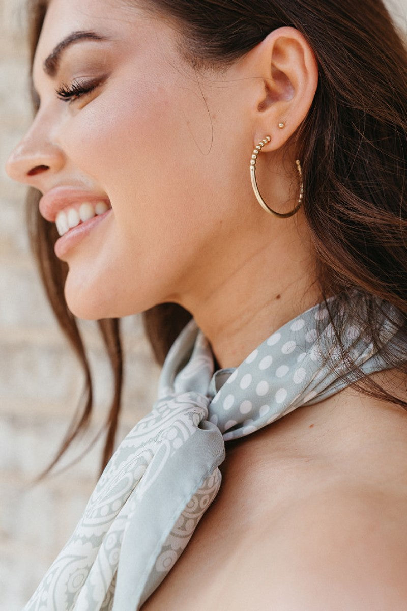 Side view of model wearing the Around The World Scarf that features light sage satin fabric with cream polka dots and paisley designs.