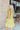 Side view of model wearing the Sweet Escape Ruffle Dress which features lime green fabric, a two-tiered body, pockets on each side, mini length, lime green lining, a square neckline, smocked details, and short ruffle sleeves.