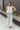 Full body front view of model wearing the Sea Breeze Pants that have white and sage sheer fabric with a marbled pattern, flared legs with a ruffle tier hem, and a  side zipper.