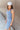 Side view of model wearing the Long Beach Dress that has light blue ribbed fabric, midi length, a round neckline, and thick straps.
