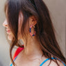 Side view of model wearing the Proud To Be Earring which features red and white stripe beads with navy blue beads and white polka dots wrapped on closed gold hoops.