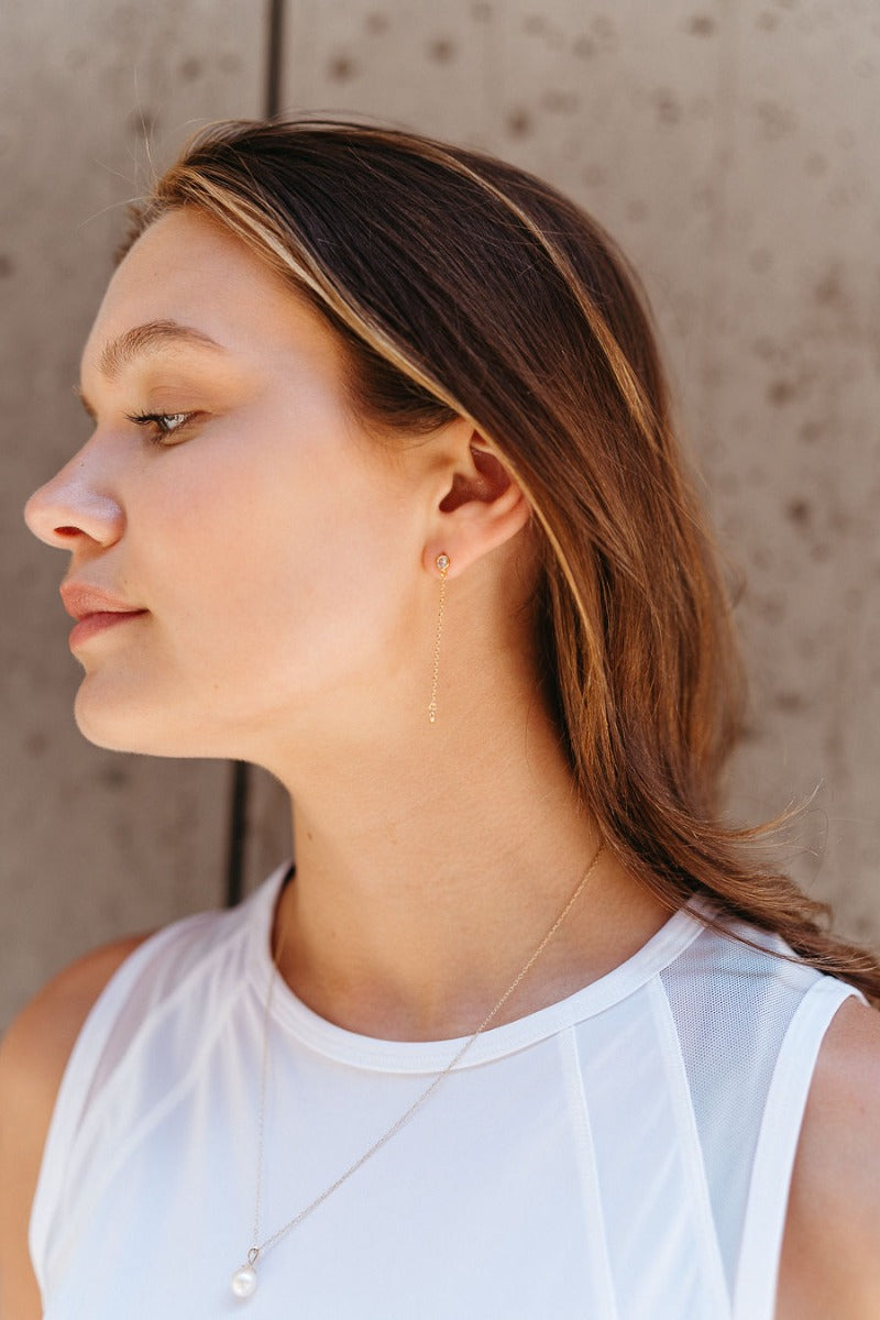 Side view of model wearing the All My Love Dangle Earring which features rhinestones linked to another rhinestone with a gold chain.