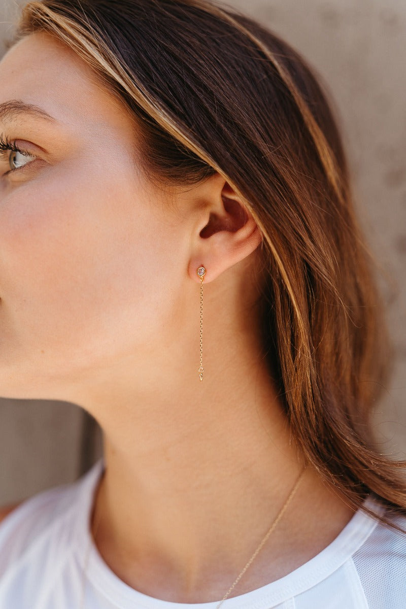 Side view of model wearing the All My Love Dangle Earring which features rhinestones linked to another rhinestone with a gold chain.