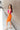 Full body side view of model wearing the Always A Dreamer Dress that has orange and fuchsia textured fabric with a color block pattern, knee length, a round neckline, and a sleeveless design.