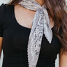 Close front view of model wearing the Happy and Free Scarf in Grey that has grey, black, and white pleated fabric with floral and paisley prints.