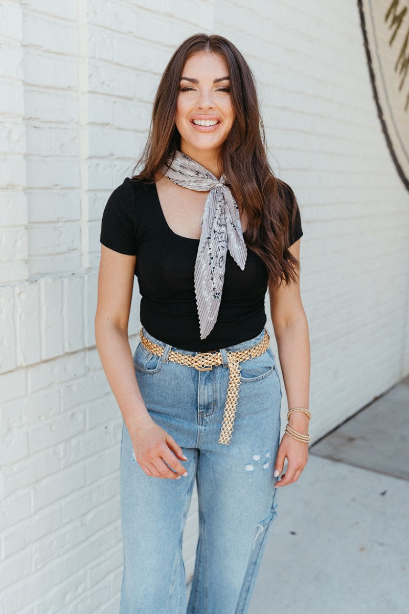 Front view of model wearing the Happy and Free Scarf in Grey that has grey, black, and white pleated fabric with floral and paisley prints.