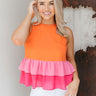 Front view of model wearing the Palm Springs Color Block Top that has orange, pink and light pink fabric with colorblock tiers, a round neck, a back keyhole with a button closure, and a sleeveless design