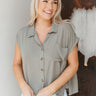 Front view of model wearing the Carpe Diem Top that has dark green fabric, dark tortoise buttons, a collared neckline, a front left chest pocket, slits on the side hem, and short sleeves