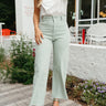 Front view of model wearing the Cross Road Jeans in Mint Green which features light sage green denim fabric, two front pockets, two back pockets, a front zipper with a monochromatic button closure, belt loops, wide legs and raw hems.