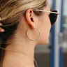 Side view of model wearing the Wrapped in You Earrings which features medium, open gold hoops wrapped with grey paper and gold details.