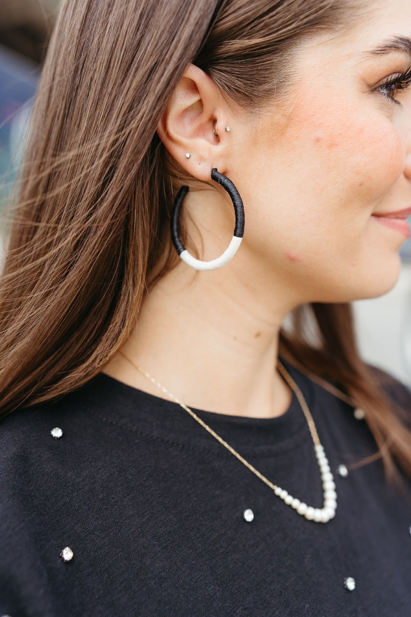 Side view of model wearing the Road Trip Hoop Earrings in Black which features large, open hoop wrapped in color-block black and white paper.