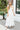 Front view of model wearing the Summer Romance Maxi Dress that has white fabric, maxi length, white lining, a ruffled hem, a plunge neckline, layered upper details, ruffle straps, and back corset ties