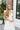 Upper front view of model wearing the Summer Romance Maxi Dress that has white fabric, maxi length, white lining, a ruffled hem, a plunge neckline, layered upper details, ruffle straps, and back corset ties