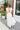 Back view of model wearing the Summer Romance Maxi Dress that has white fabric, maxi length, white lining, a ruffled hem, a plunge neckline, layered upper details, ruffle straps, and back corset ties