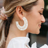 Side view of model wearing the Carolina Earrings that have large, open hoops with an ivory fringe design with gold and white beads.