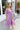 Frontal/side view of model wearing the Love Struck Floral Midi Dress that has shimmery sheer purple fabric with a blue, turquoise, and red floral print, purple lining, a ruffle hem, a square neck, and 3/4 puff sleeve with elastic trim.