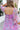 Back view of model wearing the Love Struck Floral Midi Dress that has shimmery sheer purple fabric with a blue, turquoise, and red floral print, purple lining, a ruffle hem, a square neck, and 3/4 puff sleeve with elastic trim.