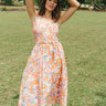 Front view of model wearing the Something Beautiful Floral Midi Dress which features an orange, pink, light pink, blue, peach, lavender and light yellow floral print, midi length, light yellow lining, a smocked upper with a square neckline, and elastic ru