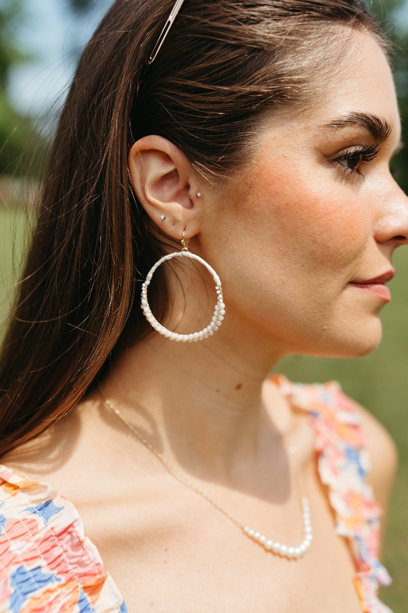 Side view of model wearing the Going Coastal Earrings that have closed, large hoops wrapped in white with white beads and gold details.