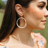 Side view of model wearing the Going Coastal Earrings that have closed, large hoops wrapped in white with white beads and gold details.