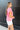 Side view of model wearing the All About Me Top which features pink gauze fabric, a square neckline, short flare sleeves, and an open back with a tie closure.