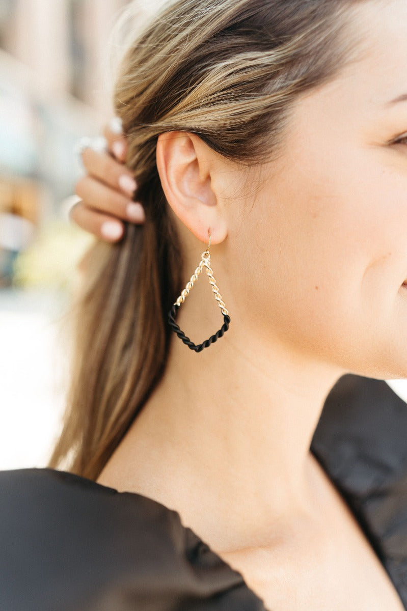 Side view of model wearing the Augustine Earrings in Black that have gold braided teardrops with colorblock black braided details.