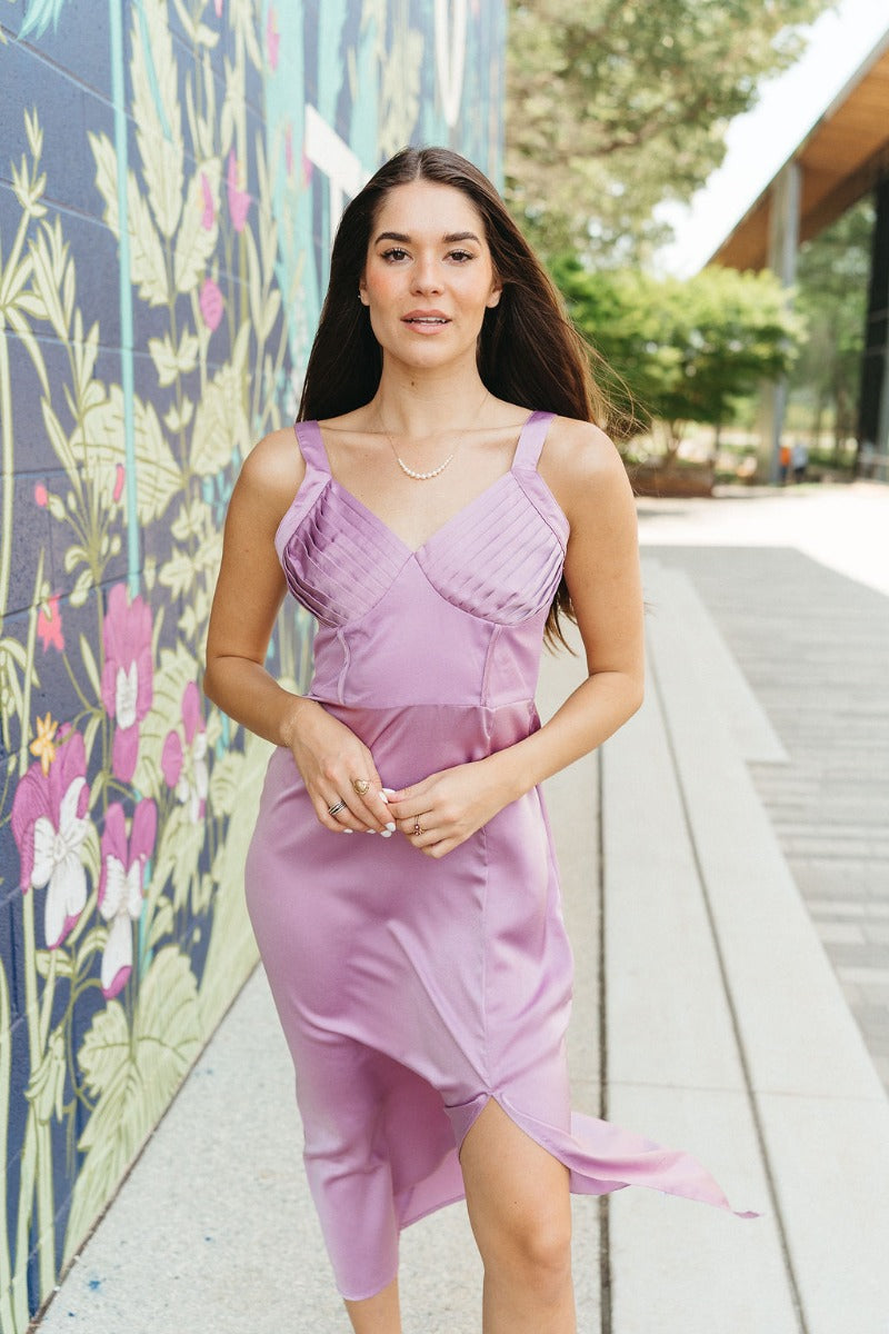 Front view of model wearing the Blaire Satin Midi Dress which features lavender satin fabric, midi length, a slit on the side, exterior boning and mesh details, pleated upper fabric, a sweetheart neckline, adjustable straps, and a monochromatic back zippe