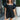 Front view of model wearing the Forever In My Heart Romper which features black fabric, a sweetheart neckline, layered ruffle short sleeves, an open back and a back tie closure.