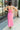 Full body back view of model wearing the One Step Ahead Midi Dress which features pink fabric, upper corset boning details, pink lining, midi length, side slits, a cowl neckline, adjustable straps, and a monochromatic back zipper with a hook closure.