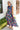 Full body front view of model wearing the Laguna Floral Maxi Dress that has a navy, orange, pink, blue, purple and green geometric/floral print, a tiered skirt, a smocked top, and a high neck with lettuce trim.