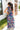 Full body back view of model wearing the Laguna Floral Maxi Dress that has a navy, orange, pink, blue, purple and green geometric/floral print, a tiered skirt, a smocked top, and a high neck with lettuce trim.