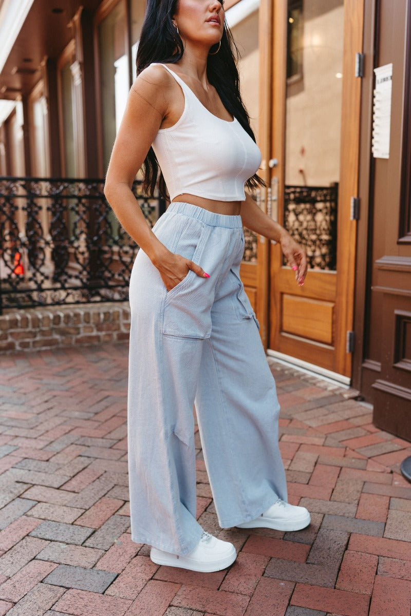 Side view of model wearing the Live Fast Cargo Pants that have light blue denim like fabric, two front pockets, an elastic waistband, and wide legs.