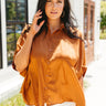 Front view of model wearing the Here With Me Top in Caramel which features caramel brown lightweight satin fabric, monochromatic button up closures, a collared neckline and short sleeves.