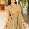 Front view of model wearing the Layla Babydoll Dress in Olive which features olive green fabric with a monochromatic checkered pattern, olive green lining, mini length, two-tiered baby doll style, a v-neckline, and short sleeves.